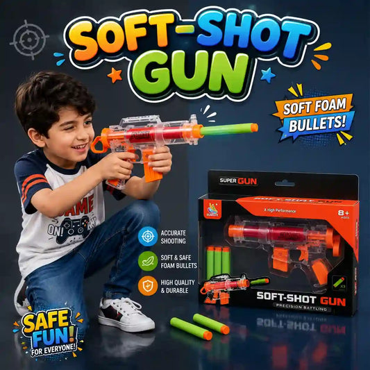 A young boy wearing a blue and white graphic t-shirt and jeans is kneeling down and smiling while aiming a soft-shot toy gun. The toy gun is clear plastic with orange and green accents.